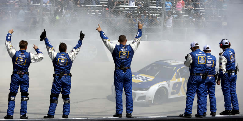 Chase Elliott celebrates with a burnout as his crew cheers from the wall