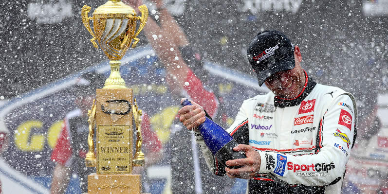 Denny Hamlin celebrates by spraying champagne in victory lane